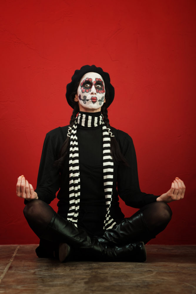 A skinny woman with All Souls Day makeup in a meditation pose